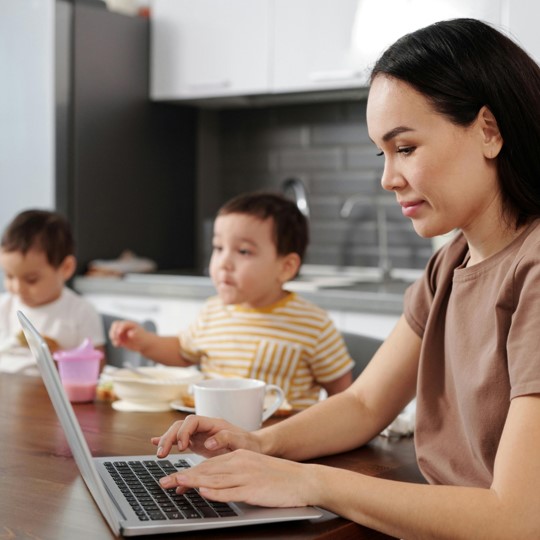 Mother job searching on her computer while her children have breakfast